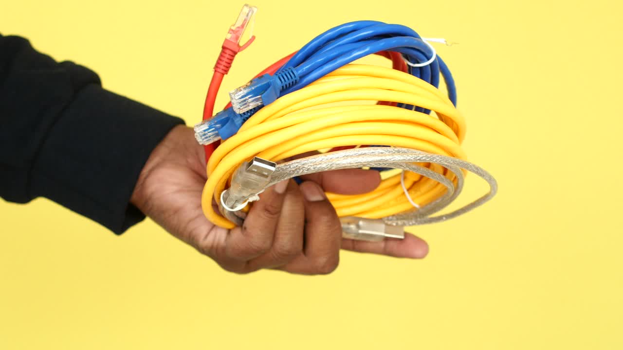 Close-up of a hand holding various cables, including network cables, USB cable, and other wires.