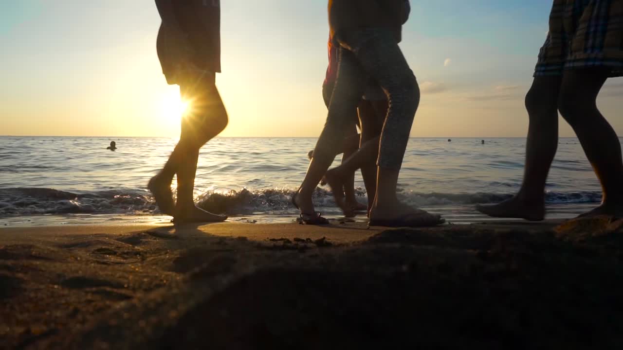 Teenagers walking by the beach while the sun is about to set and the waves are calm.
