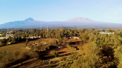 Sunrise--Kenya-landscape-with-a-village,-Kilimanjaro-and-Amboseli-national-park---tracking,-drone-aerial-view