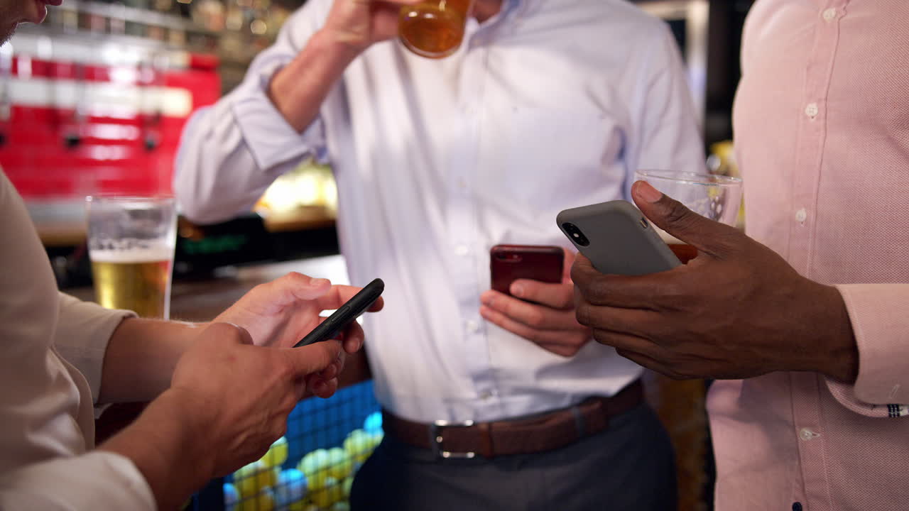 Group Of Businessmen All Checking Mobile Phones Whilst Meeting For Drink In Bar