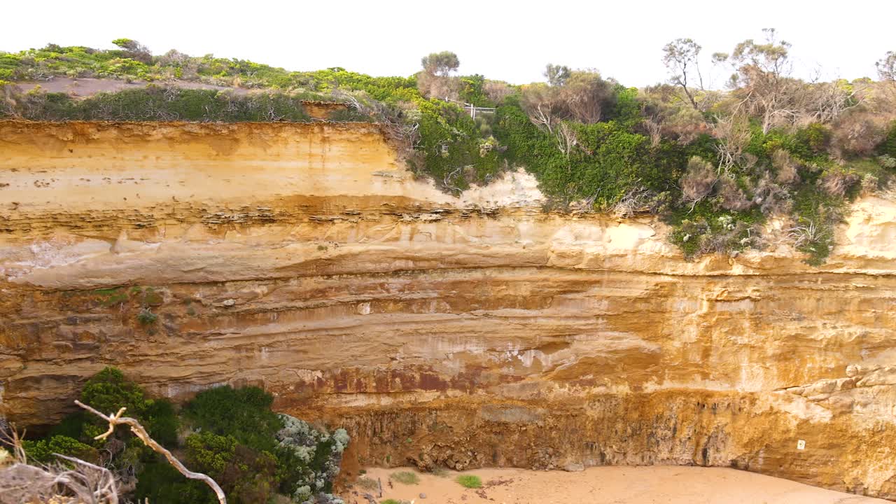 Panoramic view of Loch Ard Gorge's rugged cliffs with lush greenery under bright daylight, showcasing natural beauty and geological formations