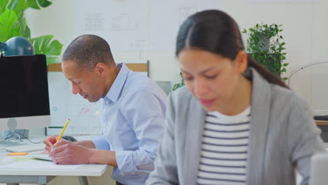 male and female architects working in office at desks on plans for new building