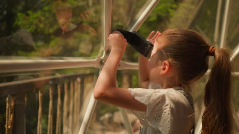 niño con cámara digital en tienda de glamping. niña pequeña dispara belleza del paisaje a través de la pared de vidrio en un día soleado. niño toma fotos del campamento