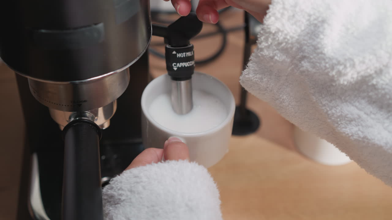 Woman whips milk for cappuccino in coffee machine. Lady in bathrobe whips milk in foam using coffeemaker cappuccinator. Process of making milk foam