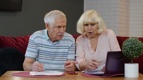 stressed senior couple discuss unpaid bank debt holding bills, doing paperwork, planning budget