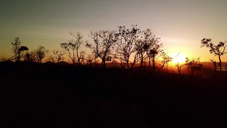 Aerial-drone-shot-of-beautiful-sunset-with-silhouette-of-trees-and-grass-in-foreground,-rising-to-show-islands-and-mountains-in-background