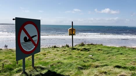 a no swimming sign on the beach in ireland west coast - in the background you can see the sea and people on the beach