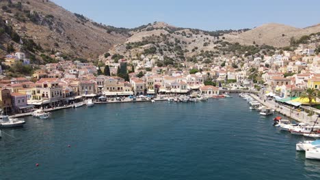 cinematic aerial from the city symi in greece to a large yacht leaving port