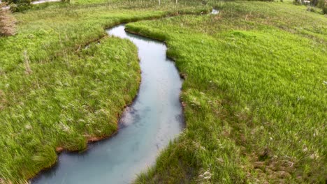 Aerial drone view of a winding blue stream flowing through vibrant green grassy marshland