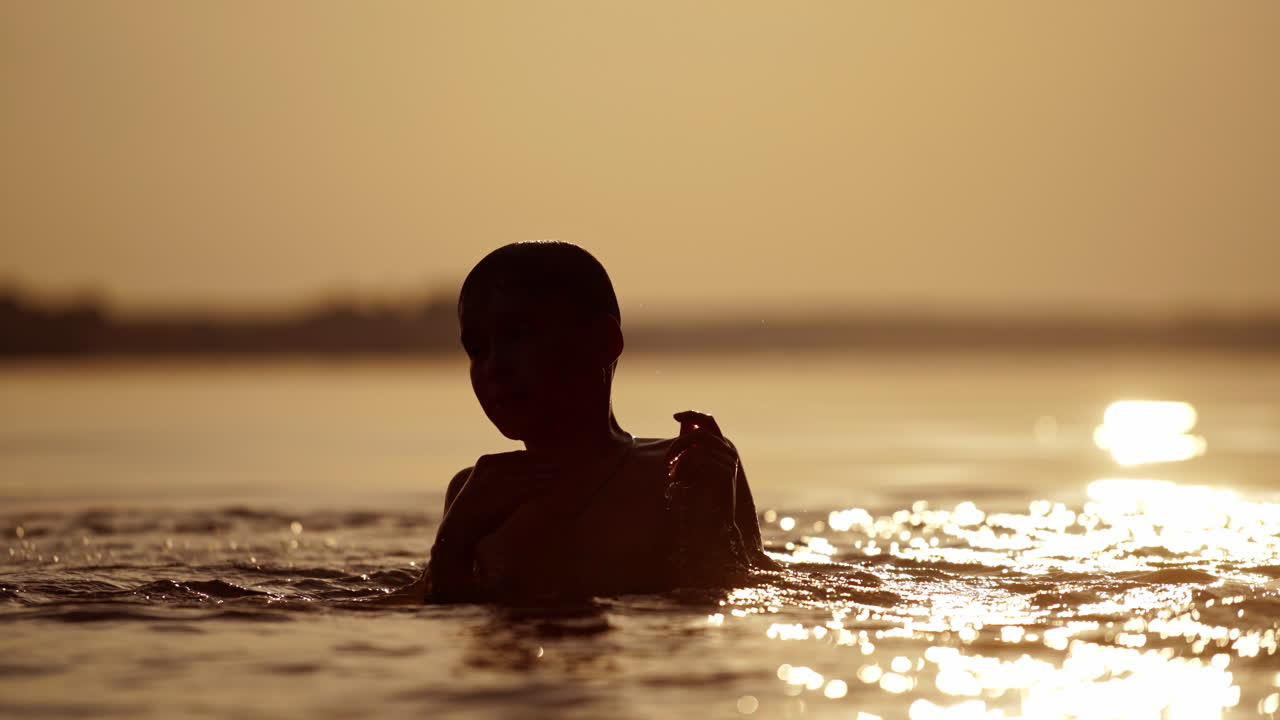 Boy swims in the river at sunset. Active child dives underwater in the evening. Silhouette of a kid swimming to his mother outdoors. Close-up.