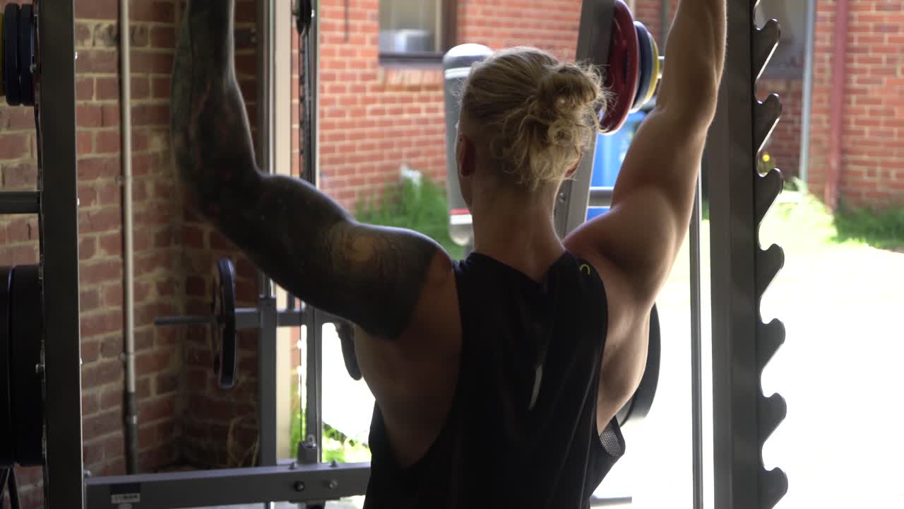 Tattoo man muscles in home gym doing single arm lat pulldowns shot from back