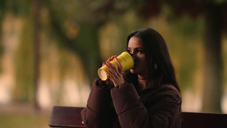 Una-Encantadora-Mujer-Moderna-Está-Bebiendo-Café-De-Una-Taza-De-Café-Desechable-En-El-Parque-Iulius,-Cluj-napoca,-Rumania