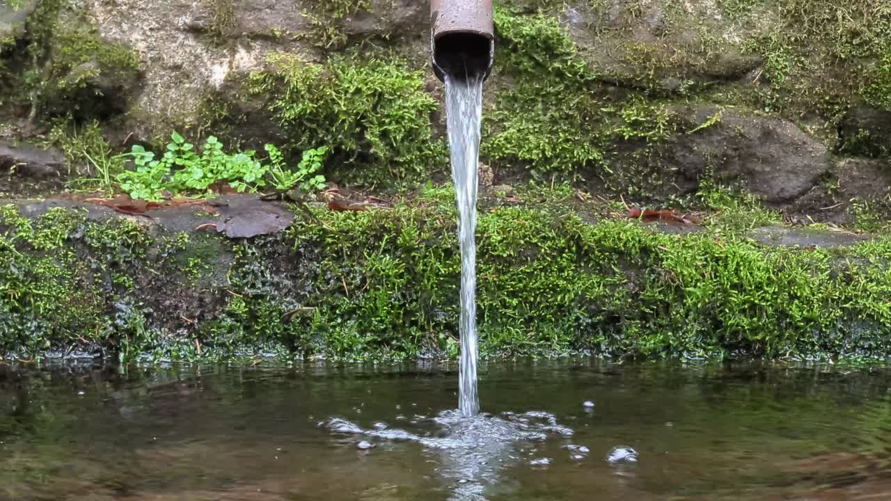 movimiento de inclinación lateral de la fuente forestal, con tubería oxidada y piedra de mampostería, el agua fluye hacia el río