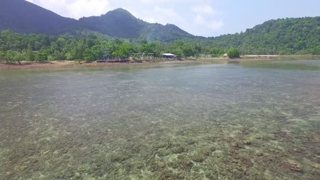 Drone-Vuela-Hacia-Atrás-Sobre-Arrecifes-De-Coral-Con-Selva-Y-Costa-En-El-Fondo