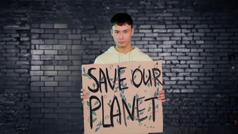 asian young environmental activist holding a cardboard with save the planet" inscription and looking at the camera"