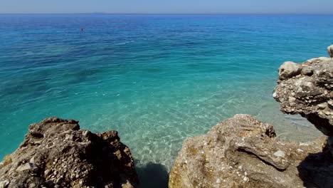 Salted-water-of-Ionian-sea-seen-through-rocks-plunged-on-beach,-blue-turquoise-colors-of-Mediterranean-in-summer