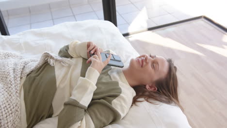 relaxing on bed, young woman smiling and using smartphone in cozy setting