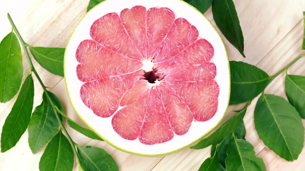 vista superior girar la fruta de pomelo roja con hojas en la mesa de madera en el jardín, la fruta del pomelo rojo con hojas con fondo de madera resolución 4k.