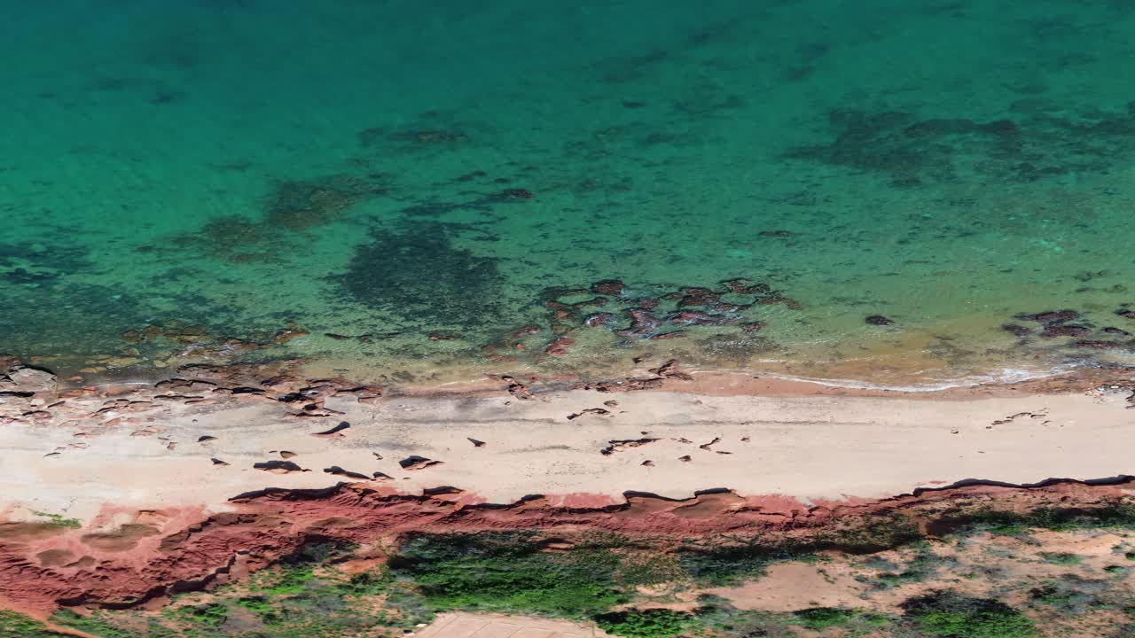 Stunning aerial shot of a remote beach in Broome, showcasing the clear turquoise waters, red sand, and unspoiled natural beauty of Western Australia's coastline.