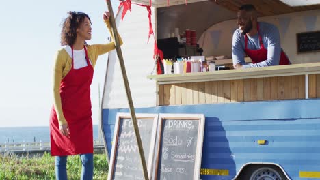 retrato de una pareja afroamericana con delantales sonriendo mientras están de pie cerca del camión de comida