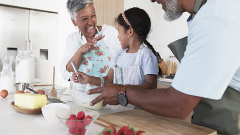 Abuelos-Birraciales-Están-Horneando-Con-Una-Niña,-Todos-Sonriendo-En-Una-Cocina-Luminosa