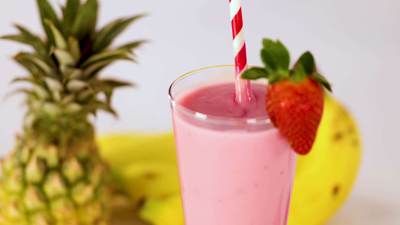 Hand reaches for pink strawberry smoothie in glass, bright lighting, tropical fruit background, static shot