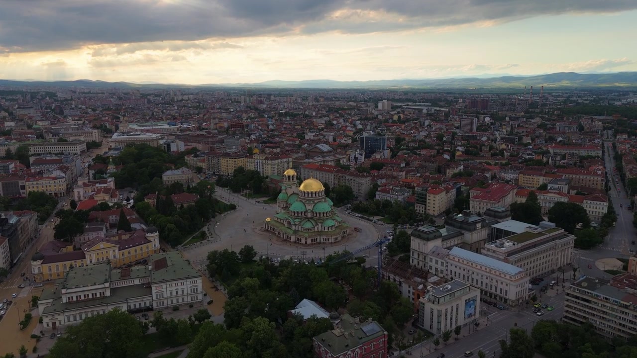 Impresionante vuelo aéreo al crepúsculo sobre la plaza central que rodea la Catedral de Alexander Nevsky, capturando el resplandor de la hora dorada sobre Sofía, Bulgaria