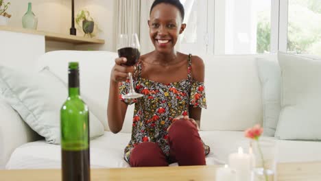 Mujer-Afroamericana-En-El-Sofá-Levantando-Una-Copa-De-Vino-Y-Sonriendo-A-La-Cámara