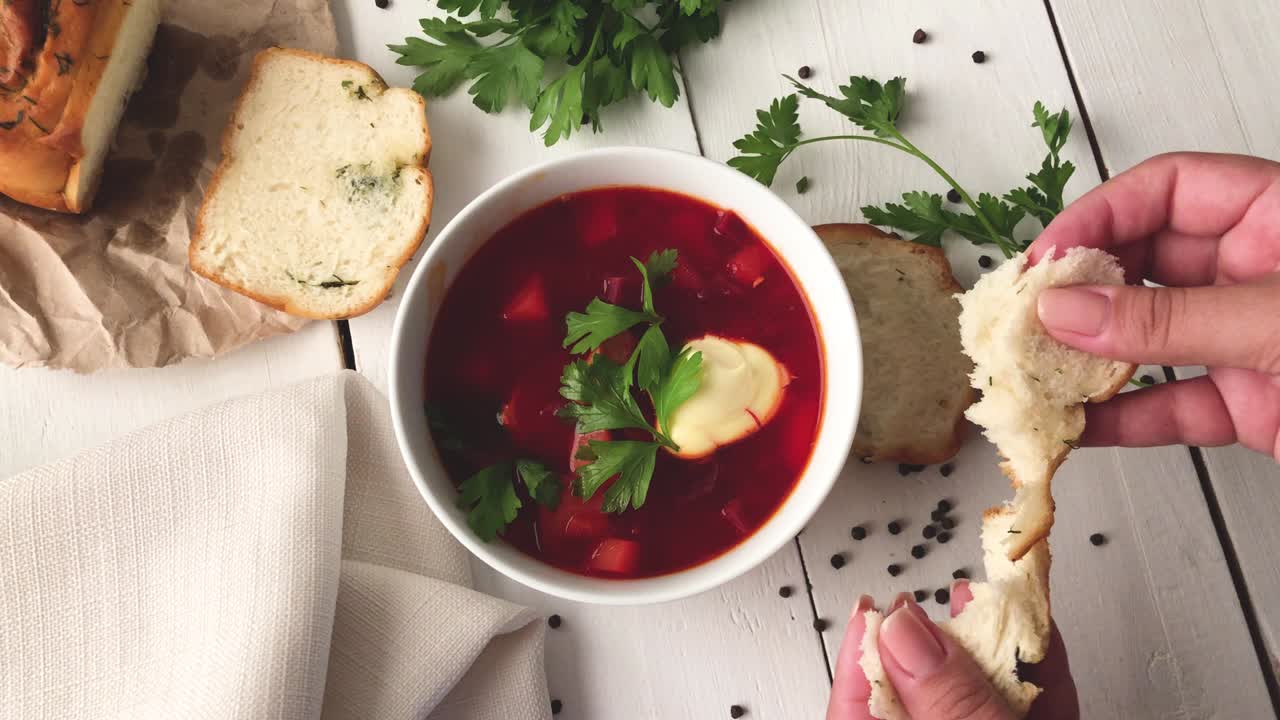 una niña rompe el pan fresco y suave cerca de un plato de sopa de remolacha vegetal