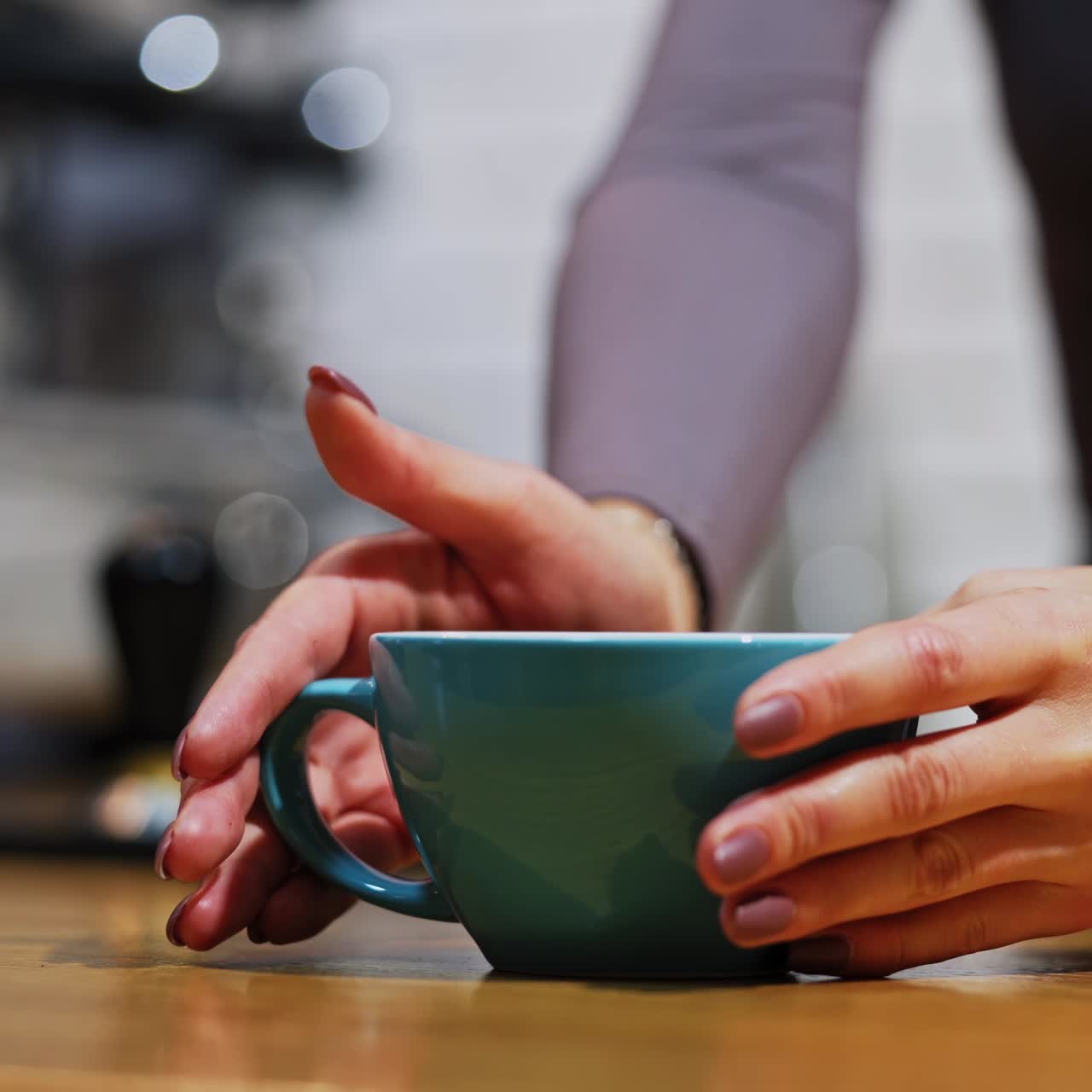 Hot drink in hands. Woman waiter putting a coffee cup with hands on table. Serving a hot drink in blue cup on blur background. Close-up.