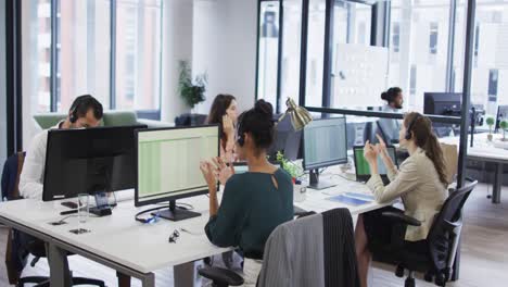 Diverse-business-colleagues-at-desks-talking-using-phone-headsets-and-computers-in-busy-office
