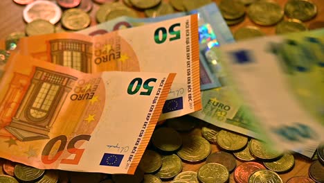 A-diverse-set-of-Euro-bills-fluttering-onto-a-table-covered-in-Euro-coins,-captured-in-a-close-up-shot