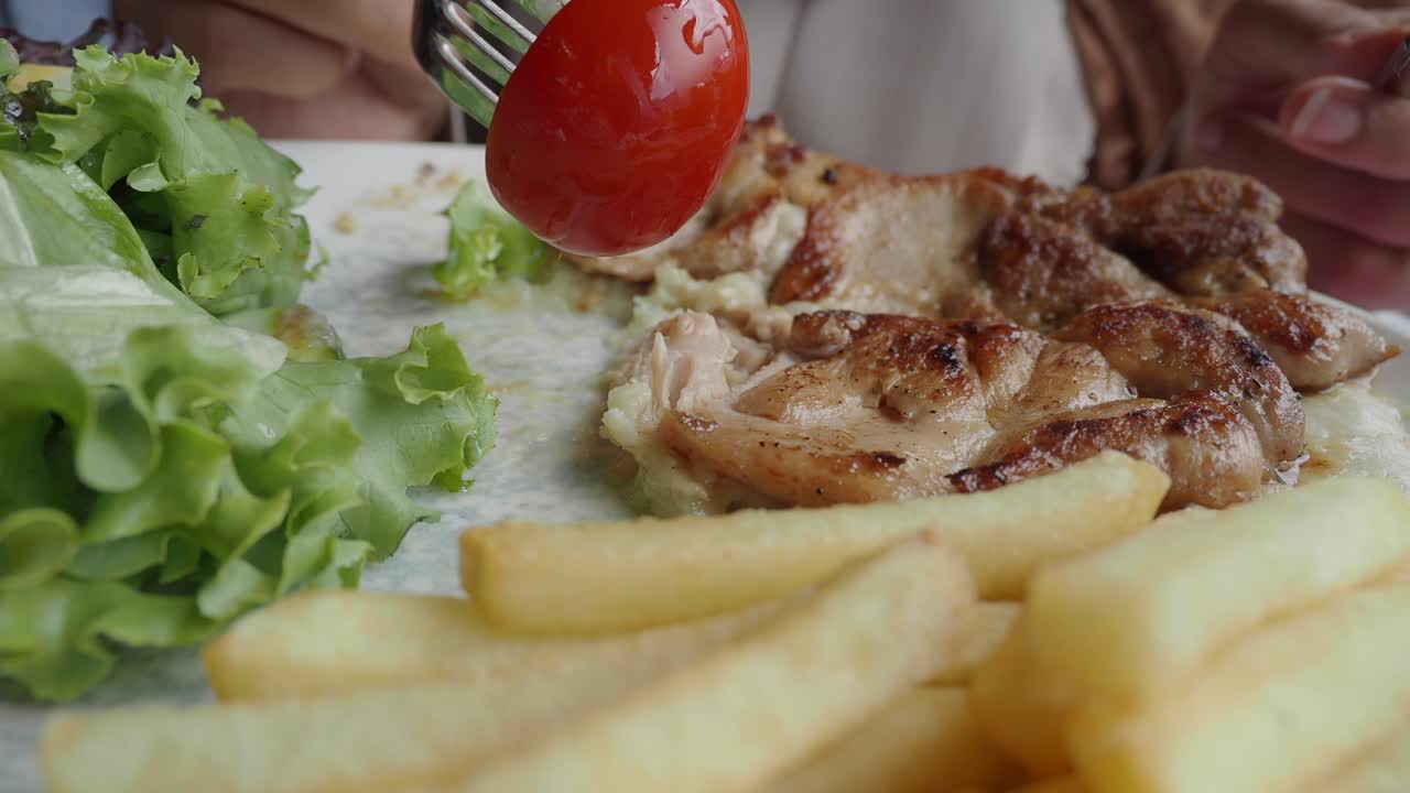 Person eating grilled chicken steak with fries and salad