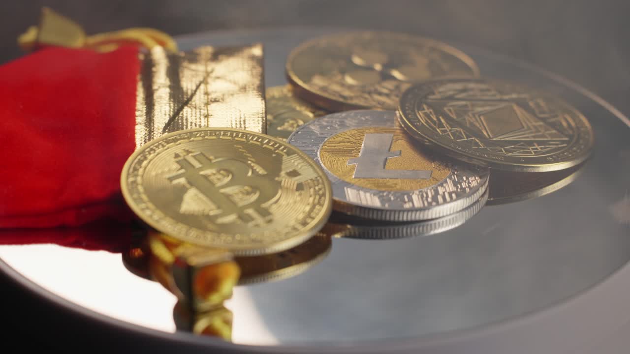 Coins symbolizing bitcoin, ripple, litecoin, and ethereum cryptocurrency slowing turning on silver turntable with red velvet bag.