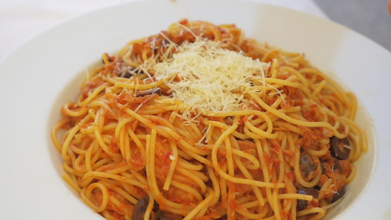 alguien rociando queso rallado en la pasta