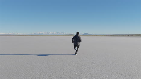 aerial view of lone man runs toward horizon across expensive salt flat, freedom and determination, mendoza, argentina