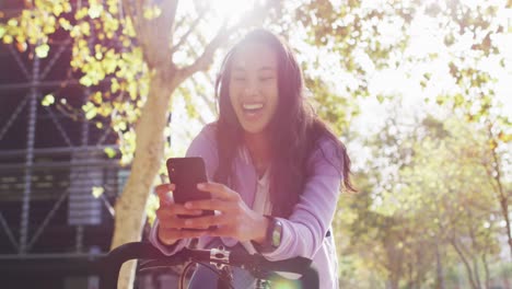 asian woman with bicycle smiling while using smartphone in the park