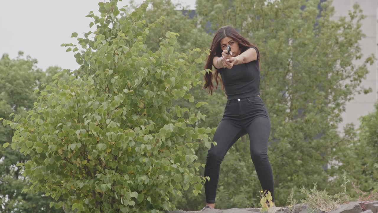 Wide view of Attractive woman aiming a pistol towards camera