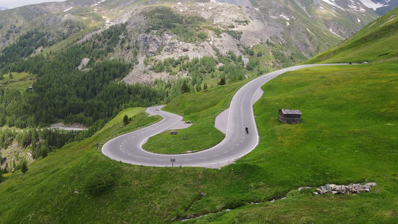 Winding alpine road unfolds through high mountains as cyclist glides down alone