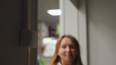 Close up of wall switch inside dim room as person opens rolling shutter and switches on light, blurred hands in background, beginning of daily service routine in business facility