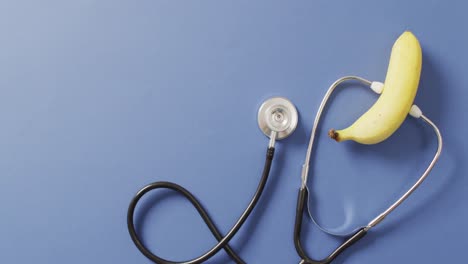 Video-of-close-up-of-stethoscope-with-banana-on-blue-background