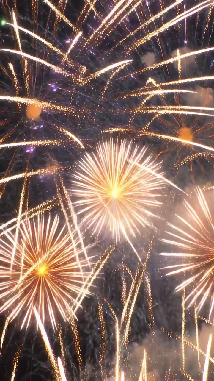 Video vertical: Lanzando cohetes, fuegos artificiales estallando para un espectáculo en el cielo oscuro, con brasas cayendo.
