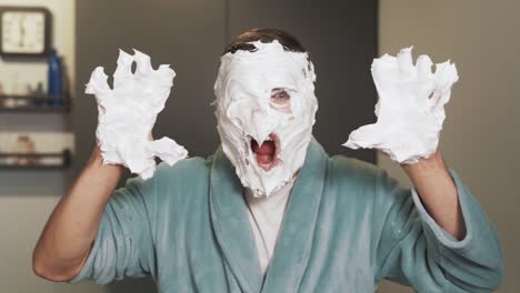 portrait of a man with foam on his face and hands scaring into the camera