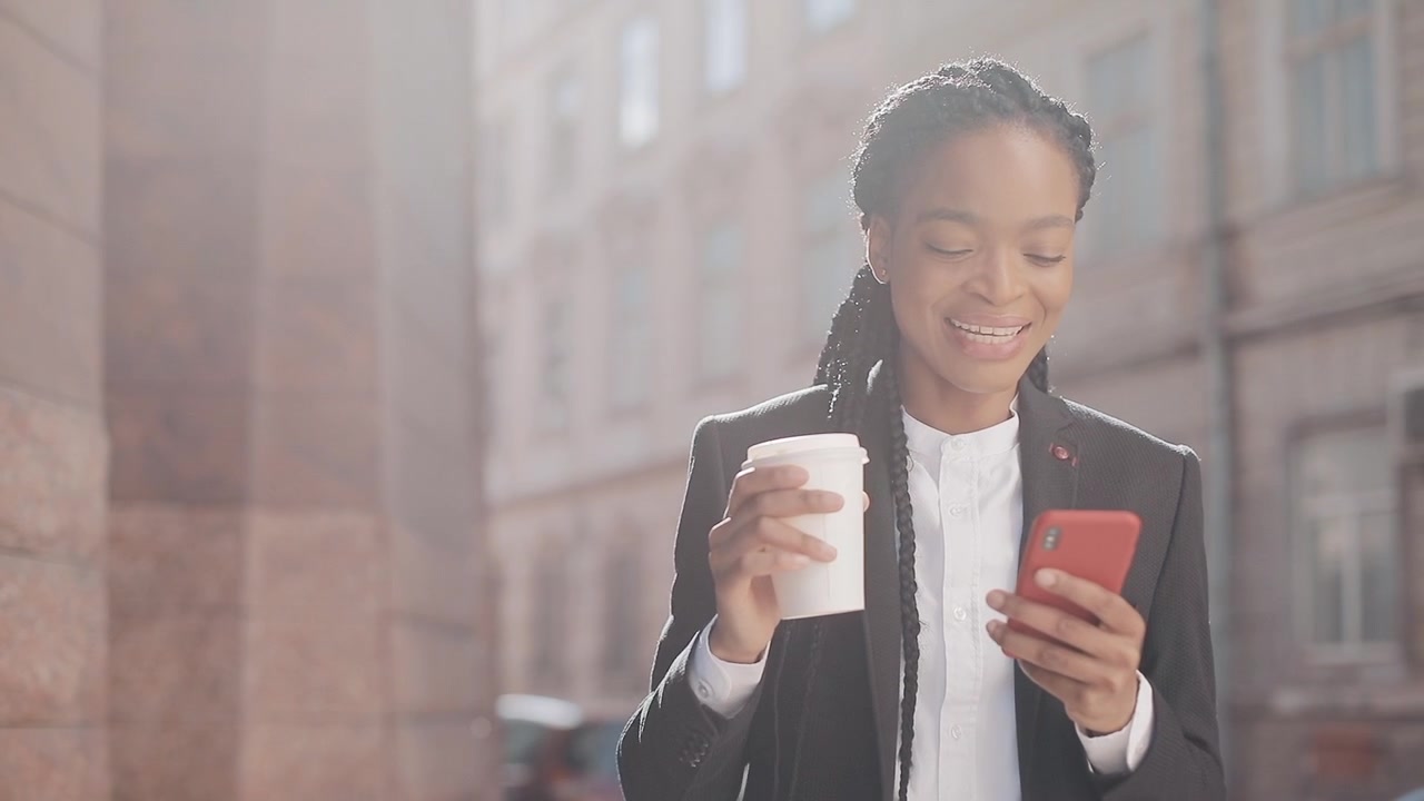 Donna d'affari sorridente che usa lo smartphone e beve caffè all'aperto