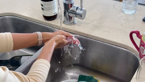 a woman thoroughly rinses her hands under running water at a modern kitchen sink, with natural daylight and steady overhead camera angle