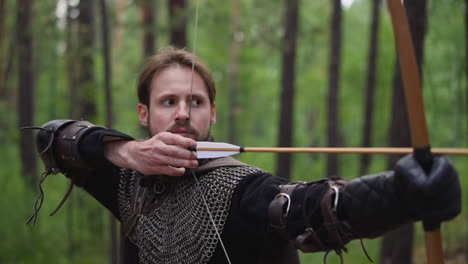 concentrated bearded archer shoots bow in green wood closeup