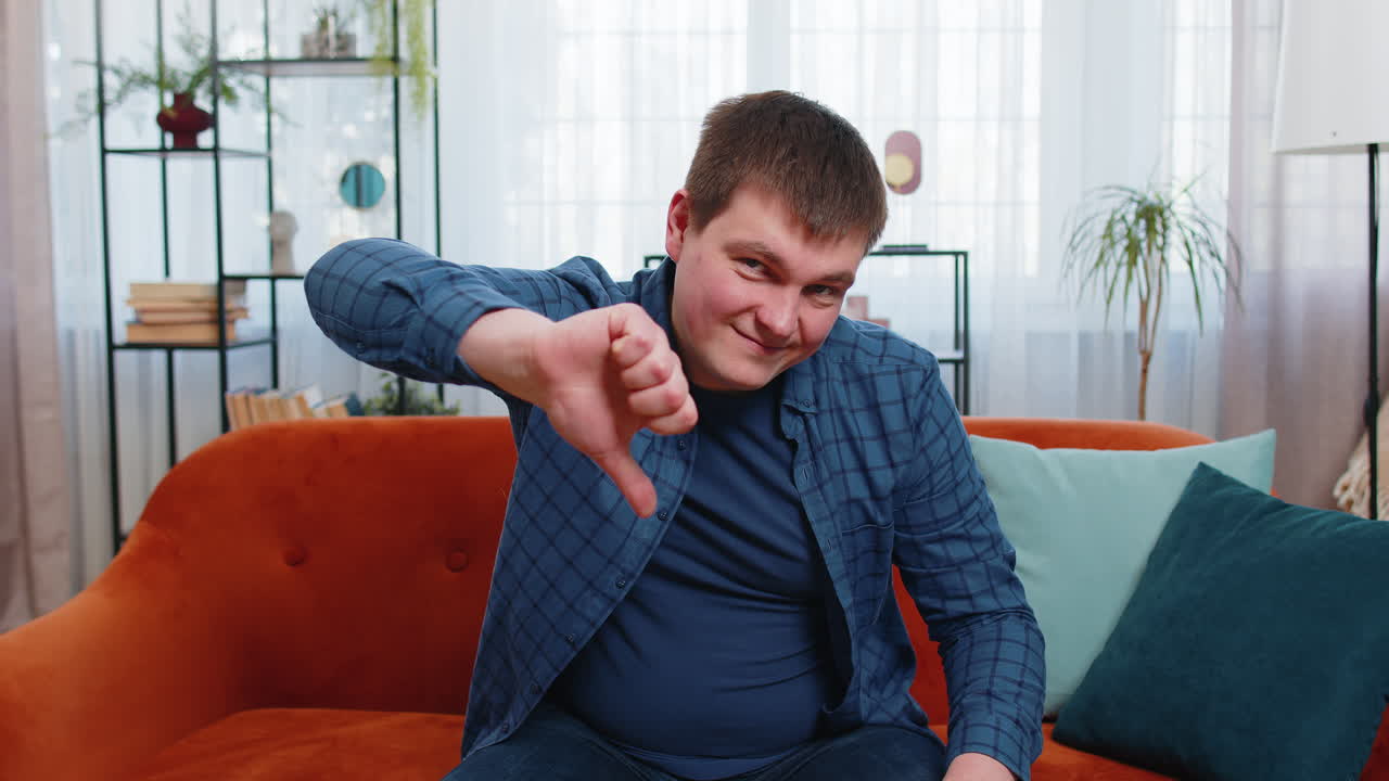 Unhappy young man showing thumb down sign gesture expressing discontent disapproval dislike bad work