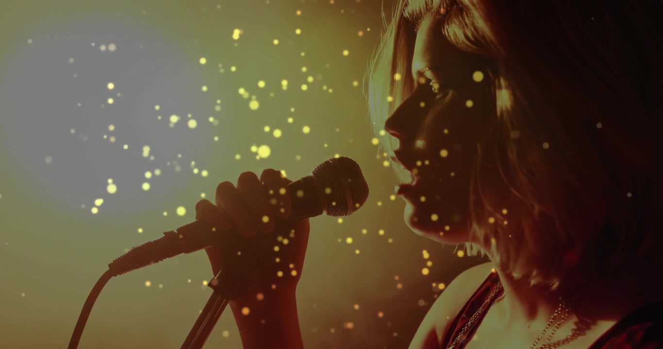 Teen singer gripping mic, leaning in, singing music while particles framing profile by stage light