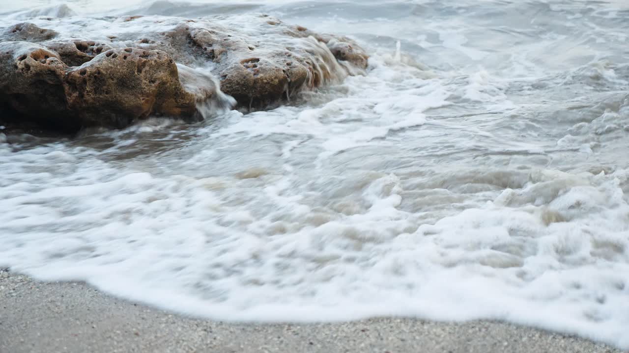 Onde che si infrangono su una roccia sulla spiaggia a tarda sera, su una spiaggia sabbiosa dell'India.