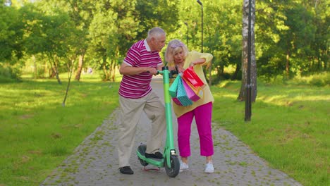 Elderly-stylish-couple-grandmother,-grandfather-after-shopping-with-bags-using-scooter-for-riding